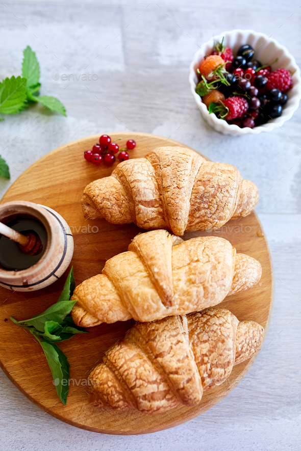 Croissants plated on a wooden tray with jam and fresh berries